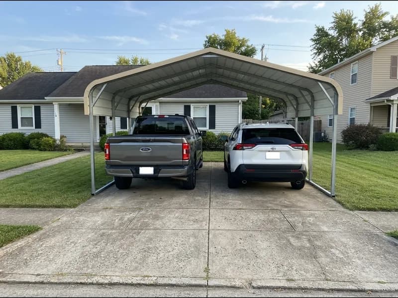 A 2023 Ford F-150 and 2022 Toyota RAV4 side by side under a 20 ft wide steel carport on a suburban driveway