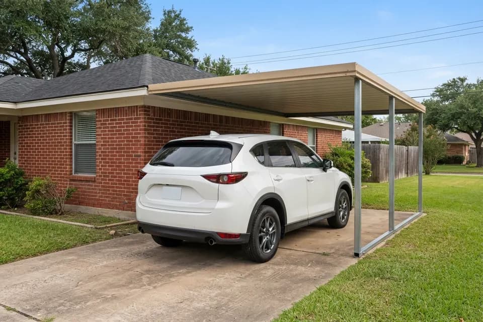 Attached steel carport on the side of a brick house sheltering a 2022 Mazda CX-5
